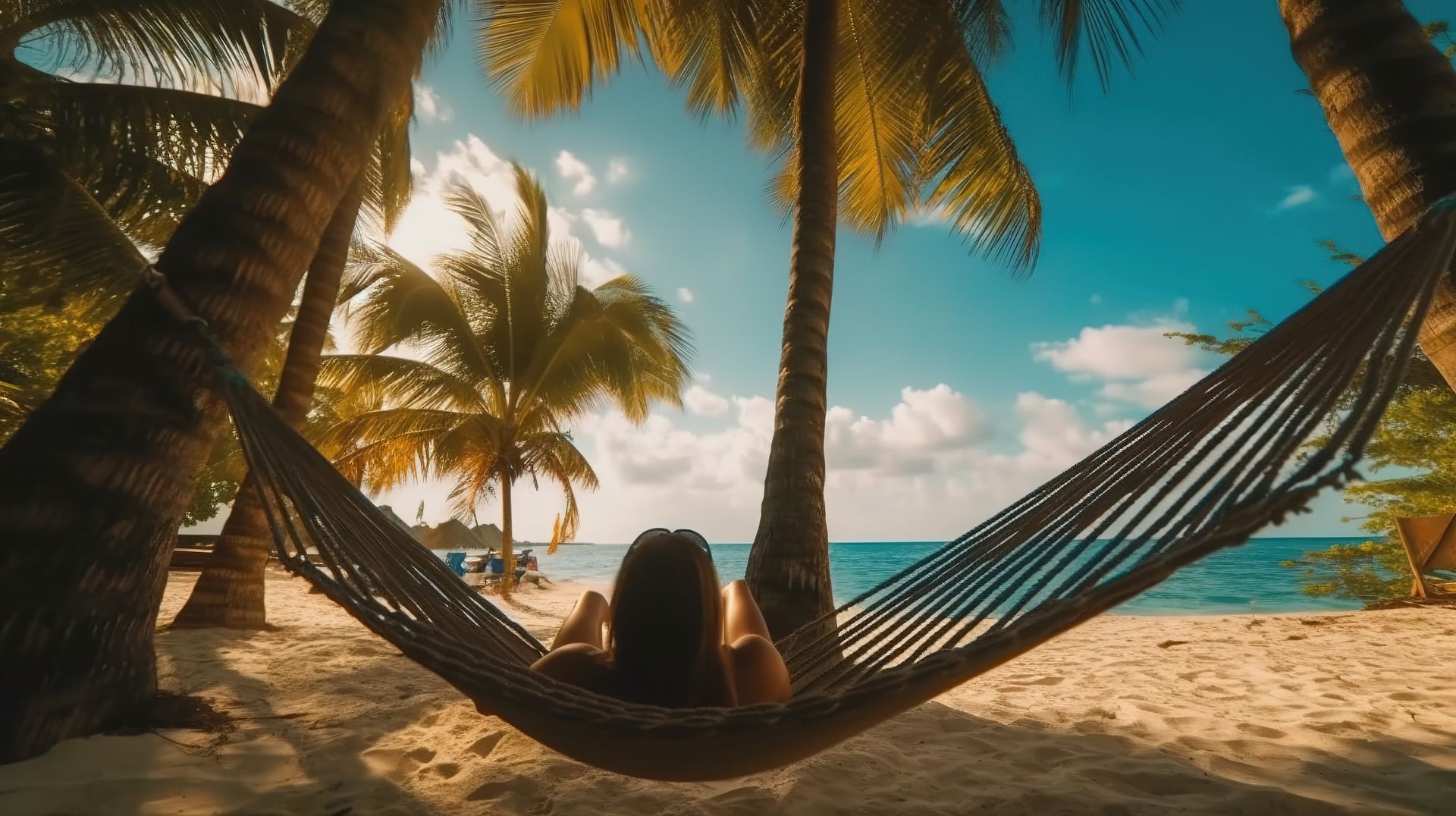 A traveler relaxing in a hammock between two palm trees above turquoise water