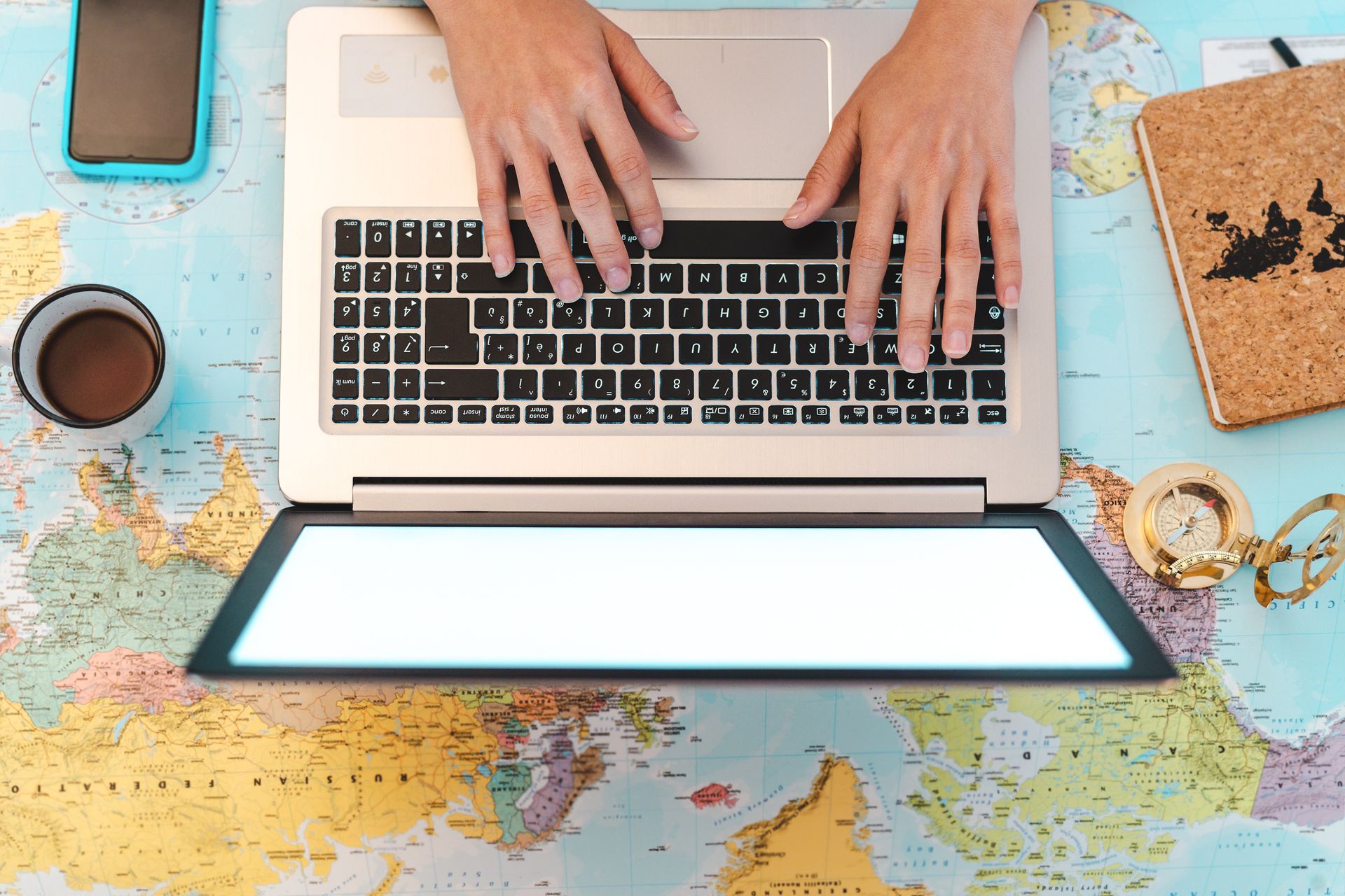 Hands on a laptop over a world map, planning the next trip